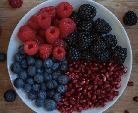 White bowl filled with blueberries, raspberries, pomegranate, and blackberries