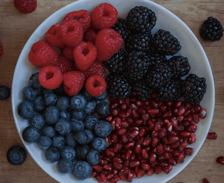White bowl filled with blueberries, raspberries, pomegranate, and blackberries