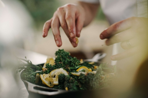 Hands sprinkling garlic in a pan of broccoli