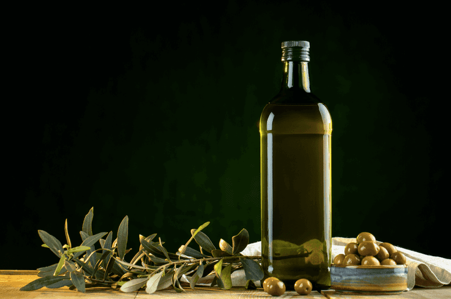 Bottle of olive oil on a table with olives.