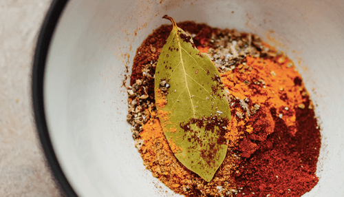Spices and a bay leaf in a white bowl