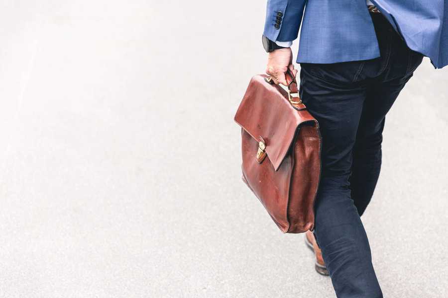 Waist down of man in suit holding leather briefcase